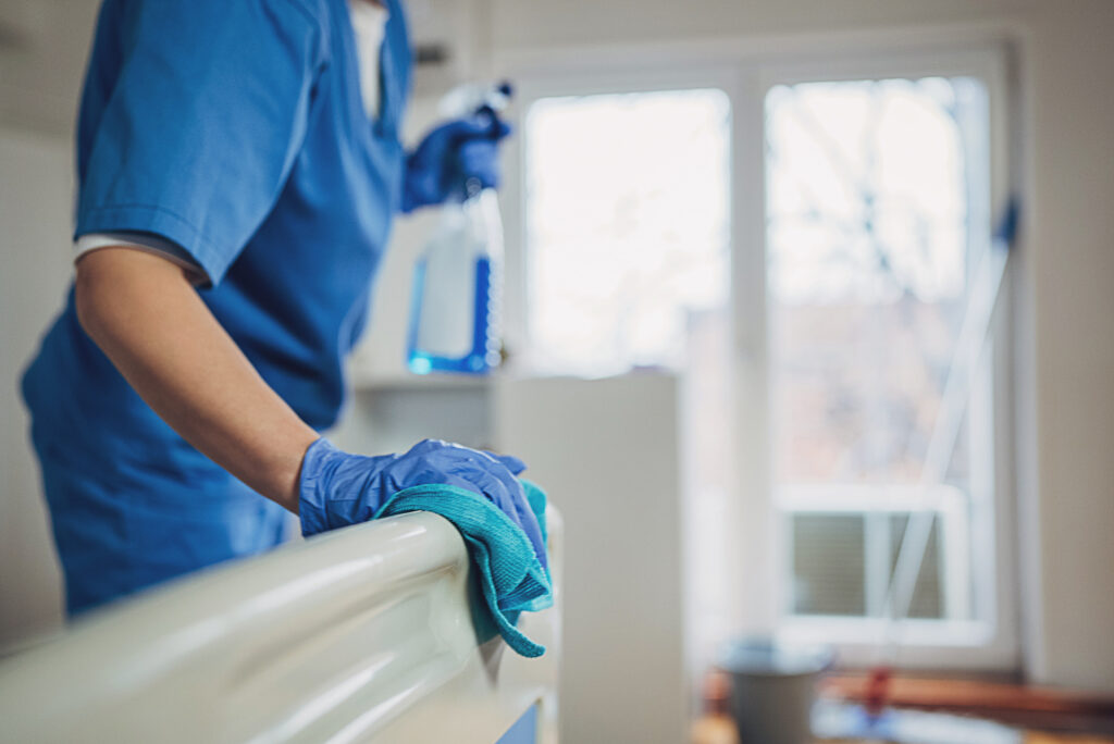 Female nurse providing cleaning services after patients in hospital ward.