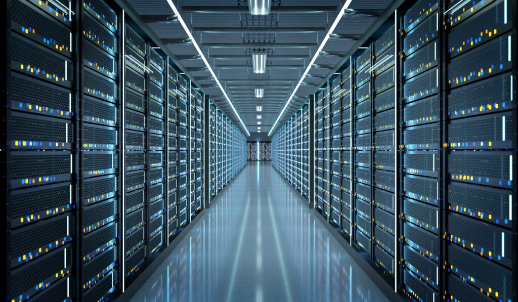 A brightly lit server room with rows of tall, black server racks on both sides, filled with blinking yellow and blue indicator lights, and a reflective floor creating a sense of depth and symmetry.